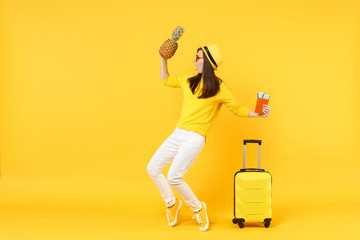 Dancing traveler tourist woman in hat holding passport tickets, fresh pineapple fruit isolated on yellow orange background. Passenger traveling abroad on weekends getaway. Air flight journey concept.