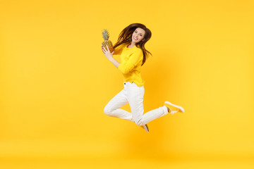 Fototapeta na wymiar Stunning young woman in casual clothes jumping, hold fresh ripe pineapple fruit isolated on yellow orange wall background in studio. People vivid lifestyle, relax vacation concept. Mock up copy space.