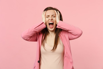 Screaming young woman wearing jacket keeping eyes closed and putting hands on head isolated on pastel pink wall background in studio. People sincere emotions, lifestyle concept. Mock up copy space.