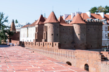 Fototapeta premium Warsaw, Poland Famous Barbican old town historic cobblestone street in capital city during sunny summer day and red orange brick wall fortress architecture