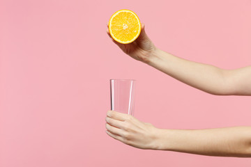 Close up cropped photo of female holding in hands half of fresh ripe orange fruit, glass cup isolated on pink pastel wall background. People vivid lifestyle relax vacation concept. Mock up copy space.