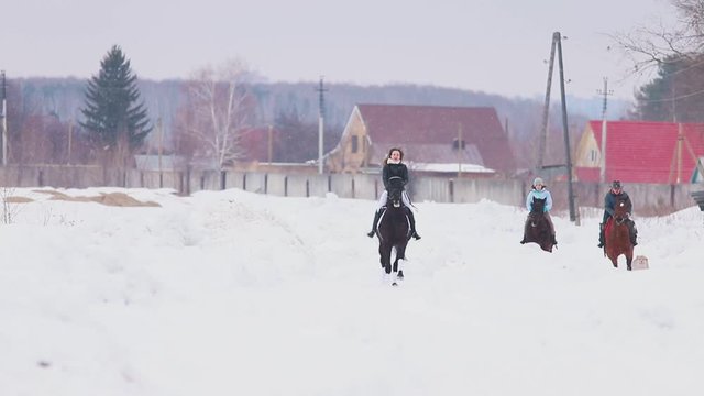 Winter time. Three women riding horses in a village with a dog running near by them