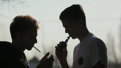Silhouette of two talkative boys that smoking and vaping outdoors