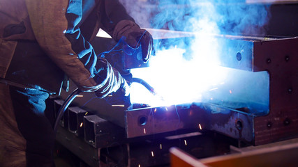 A man at the construction plant using a welding machine. Bright blue lighting