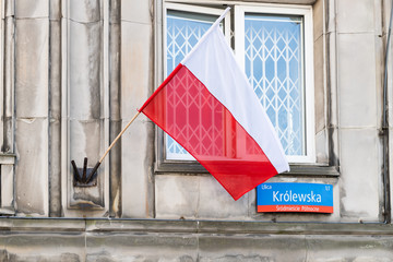 Closeup of Polish red flag in old town historic street during sunny summer day and Krolewska street sign Warsaw, Poland