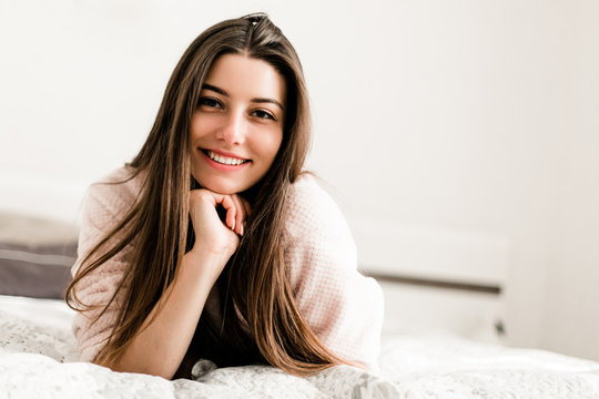 Young smiling woman lying in bed in her bedroom. Happy morning.