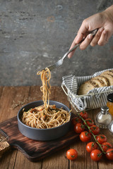 Spaghetti is pulled up by the fork in hand from dish and wooden plate for serving with homemade environment on classic, rustic background. side view, perspective, vertical, pouring shots, image