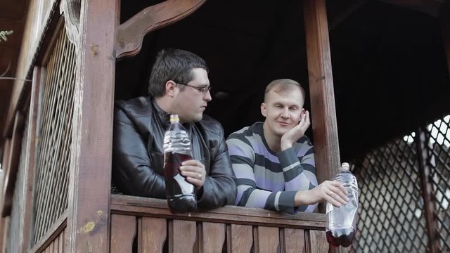 Two men on terrace drink beer from plastic bottles and speaking