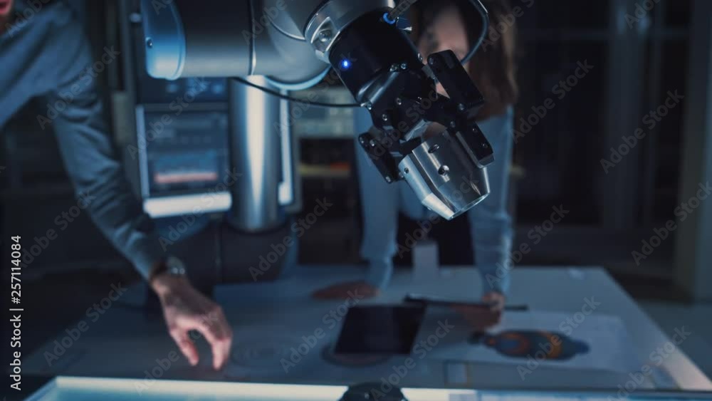 Poster close up of a futuristic robotic arm picking up a metal object and moving it. team of engineers foll