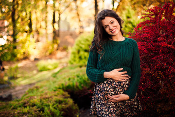 Beautiful pregnant woman posing on red tree leaf background.