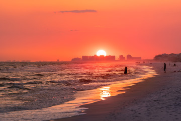Shore with dramatic orange red pink sunset in Santa Rosa Beach, Florida with Pensacola coastline coast cityscape skyline in panhandle with ocean gulf mexico waves