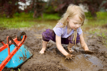 Funny little girl playing in a large wet mud puddle on sunny summer day. Child getting dirty while...