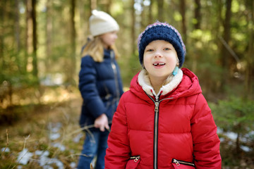 Two cute young sisters having fun during forest hike on beautiful winter day. Active family leisure with kids.