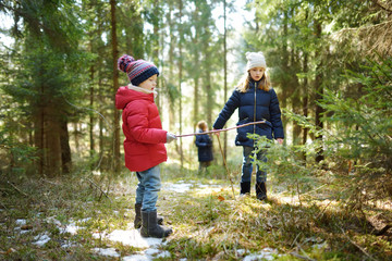 Two cute young sisters having fun during forest hike on beautiful winter day. Active family leisure with kids.