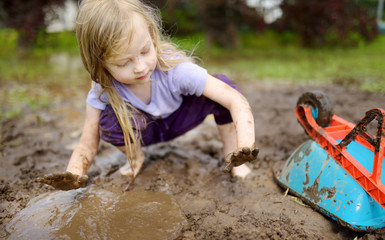 Funny little girl playing in a large wet mud puddle on sunny summer day. Child getting dirty while...