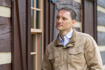 Young handsome attractive happy man face closeup with by rustic farm wooden house farmer in backyard or garden spring autumn summer background portrait in jacket coat brown