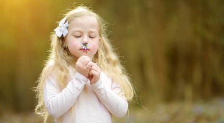 Adorable little girl picking the first flowers of spring in the woods on beautiful sunny spring day.