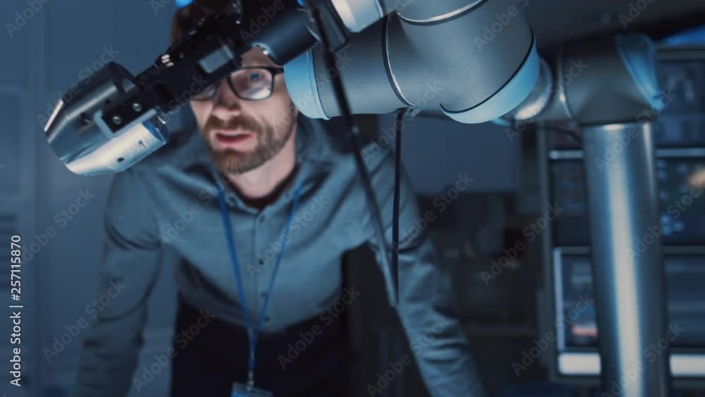Poster close up of a futuristic robotic arm moving a metal object and placing it. team of engineers discuss