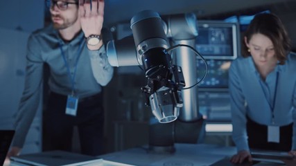 Futuristic Metal Robotic Arm Picking Up a Metal Object and Moving It. Senior Engineer Talks Through This Advanced Process. They are in a High Tech Research Laboratory with Modern Equipment. - Powered by Adobe