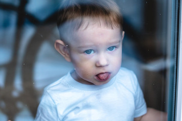 Cute baby boy looking in the window glass. Loneliness of children and waiting for kindness....