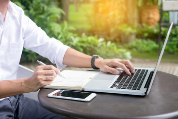 Man working on modern laptop sitting outside natural hardwood desk with green flora background sunlight day outdoor, everywhere you are from laptop concept.