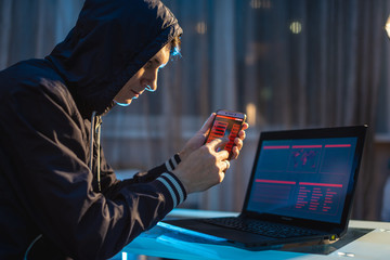 Male hacker in the hood holding the phone in his hands trying to steal access databases. Concept of...