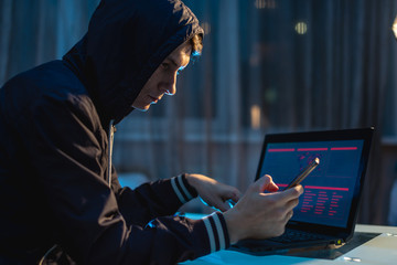 Male hacker in the hood holding the phone in his hands trying to steal access databases. Concept of...