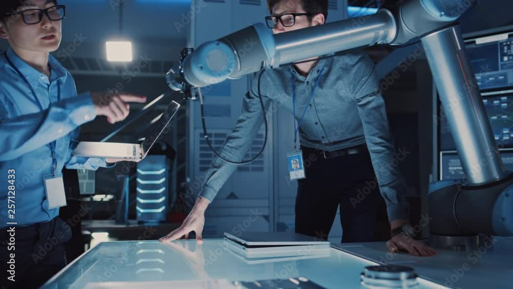 Fototapete diverse team of engineers with laptop and a tablet analyse and discuss how a futuristic robotic arm 