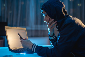 Cybercriminal in the hood typing program code while stealing access databases with passwords....