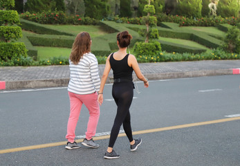 Obraz premium Closeup of young and old Asian women, daughter and mother walking in the track on the road of public park in the evening. Good exercise and recreation for own health promotion. 
