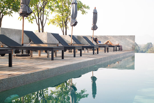 Kanchanaburi, Thailand - February 20, 2019 : Modern and simply design chaise lounge and swimming pool on the hotel roof top with mountain view with bikini girl relaxing
