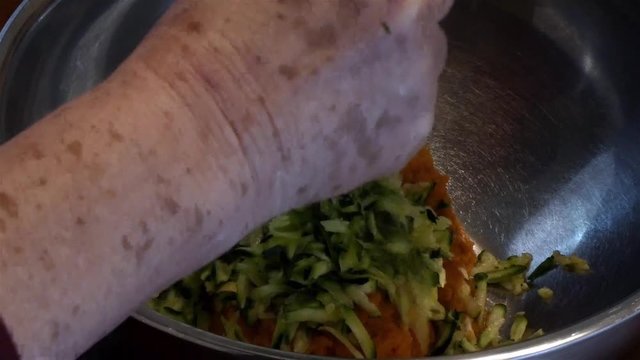 adding shredded zukini into a silver bowl
