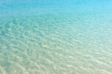 Clear blue water ripple on sandy beach. Sea water reflections surface. Tropical sunny summer day.