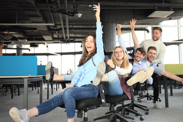 Young cheerful business people dressed in casual clothing are having fun on rowing chairs in a modern office.
