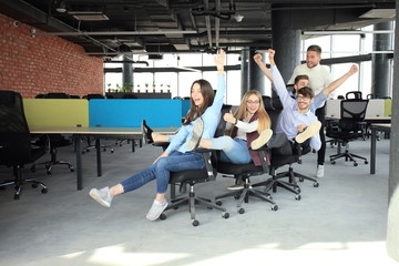 Young cheerful business people dressed in casual clothing are having fun on rowing chairs in a modern office.