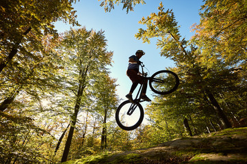 Man cyclist jumping on trial bicycle, professional rider making acrobatic trick on big boulder in the forest on summer sunny day. Concept of extreme sport active lifestyle