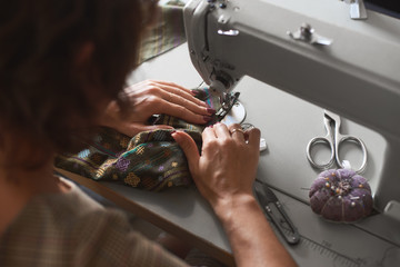 Close-up of female seamstress hands sewing clothing detail on electrical sewing machine. Tailor atelier - handmade exclusive clothes making and repair, private business, creative occupation concept.