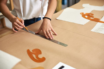 Workplace in design studio. Professional female designer hands close-up making paper patterns using measuring tape, ruler and curves. Exclusive clothes making, creative occupation concept.