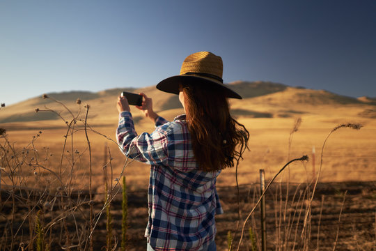 skinny girl wearing hat taking photo of rural california landscape