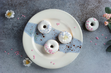Donatos buns or donuts with icing on a plate. The composition is complemented by flowers. Light background. Close-up. View from above.