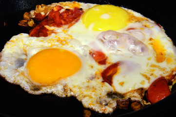 Fried eggs with colorful yolks and tomatoes. In the form of the artist's palette. Fried on a black cast iron skillet.