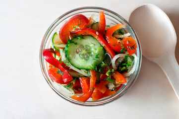 Fitness salad with tomato, cucumber, onion, pepper, dill, parsley, olive oil, spice. Vegetable salad on wooden table. Wooden spoon.
