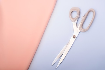 Sewing tools: pink fabric and scissors, on a blue background (top view, flat lay)