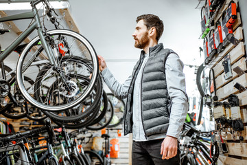 Man choosing new bicycle to buy standing in the shop with lots of bicycles and sports equipment indoors