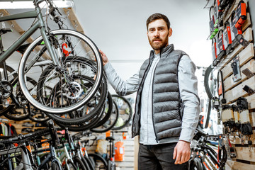 Man choosing new bicycle to buy standing in the shop with lots of bicycles and sports equipment...