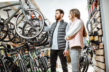 Salesman helping young woman to choose a new bicycle to buy standing in the bicycle shop