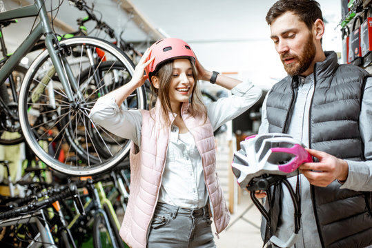 Young woman customer choosing protective helmet standing with salesman in the bicycle shop