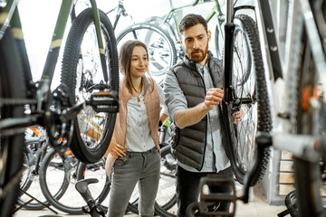Salesman helping young woman to choose a new bicycle to buy standing in the bicycle shop
