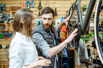 Salesman helping young woman to choose a new bicycle to buy standing together in the bicycle shop