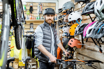 Portrait of a handsome man as a buyer or saleperson standing bicycle near the protective helmets at the bicycle shop